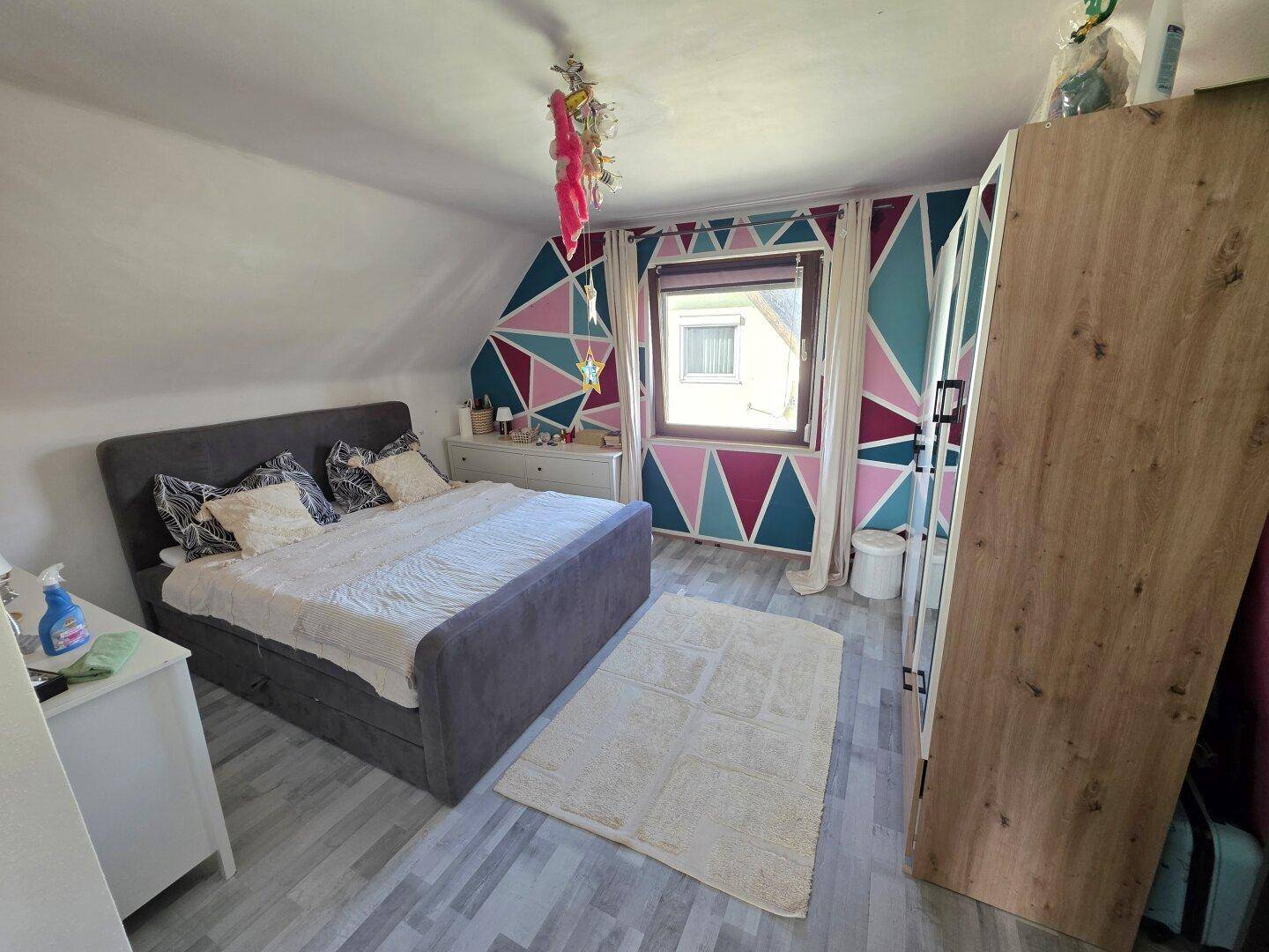 Schlafzimmer mit Doppelbett, Holzkleiderschrank und farbenfroher geometrischer Wandgestaltung.
