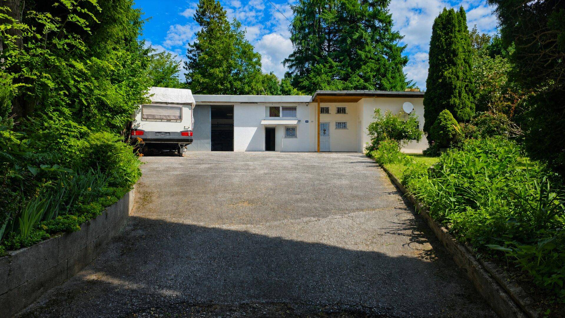 Zufahrt zum Haus mit Stellplatz und umgebender Bepflanzung.