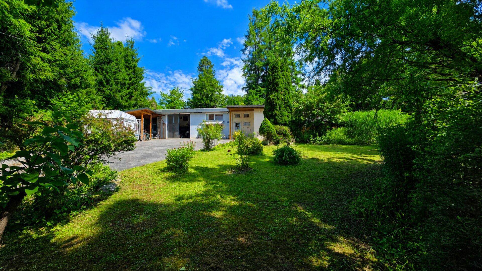Vorderansicht des Hauses mit weitläufigem Rasen und umgebenden Bäumen.