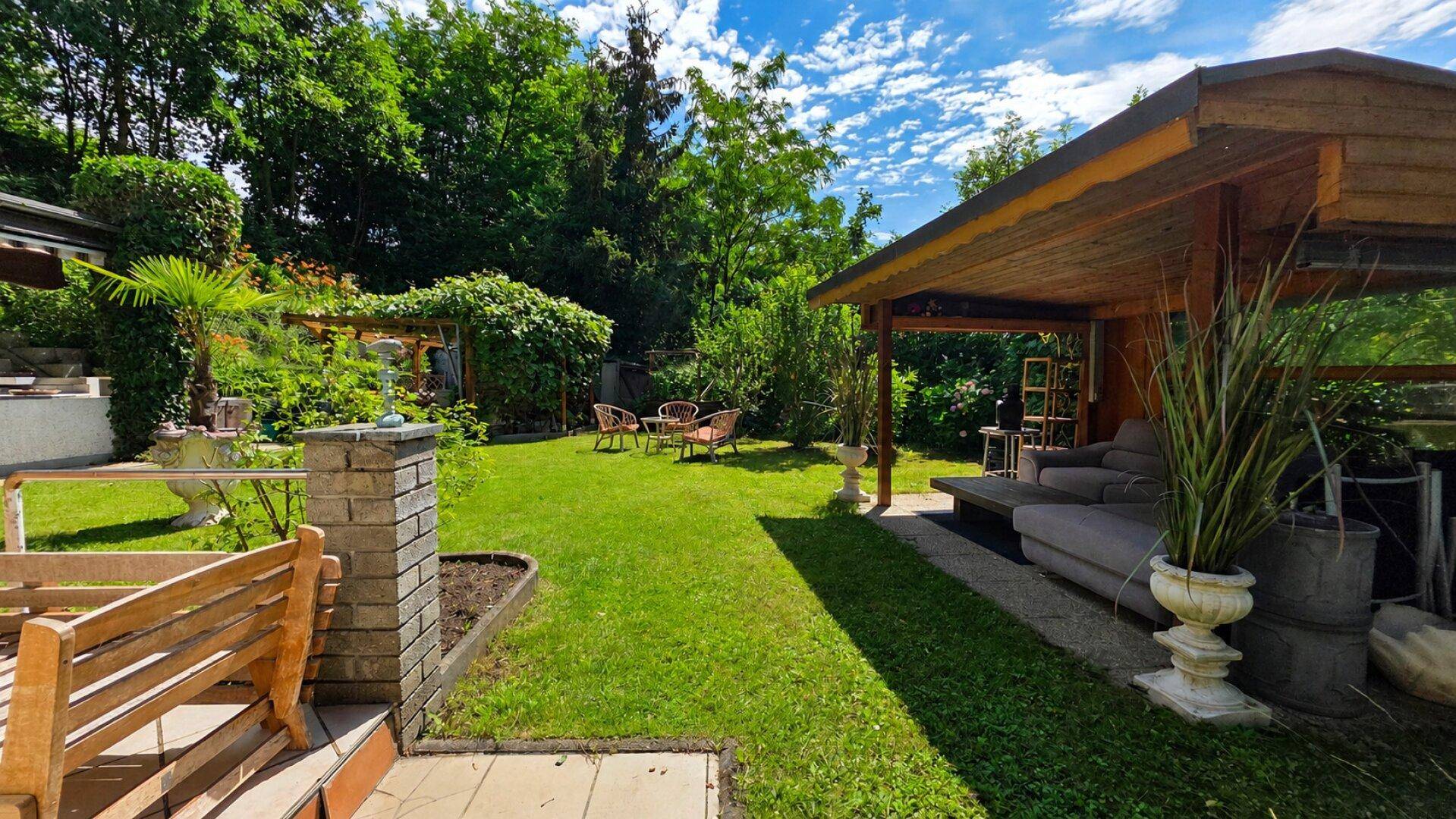 Gepflegter Garten mit Rasenfläche, überdachtem Loungebereich und weiteren Sitzgelegenheiten.