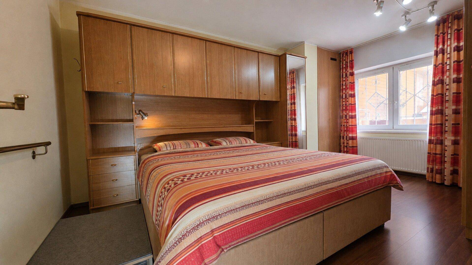 Schlafzimmer mit großem Bett, Einbauschränken aus Holz und farbigen Vorhängen.