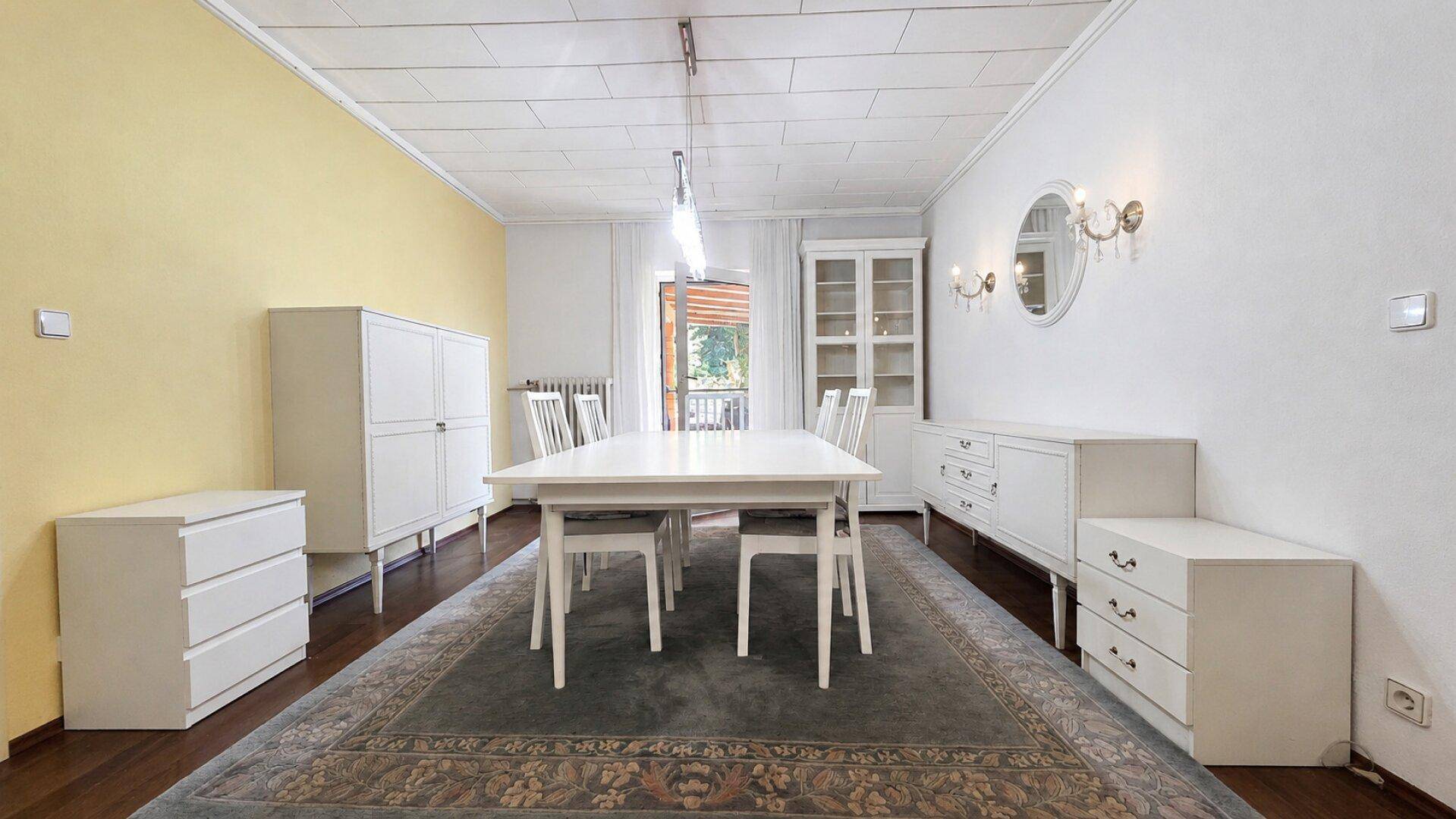 Helles Esszimmer mit langem weißen Esstisch, passenden Stühlen und Sideboards.