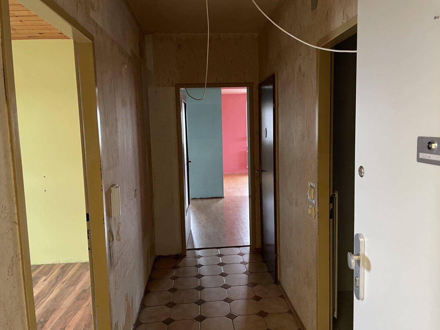 Flur mit Fliesenboden und mehreren Türen, der in verschiedene, renovierungsbedürftige Räume führt.