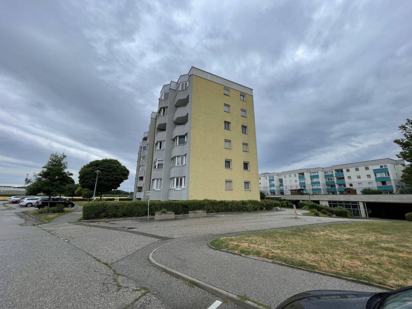 Mehrfamilienhaus mit gelber Fassade und Balkonen in einer Wohnsiedlung mit Parkplätzen.