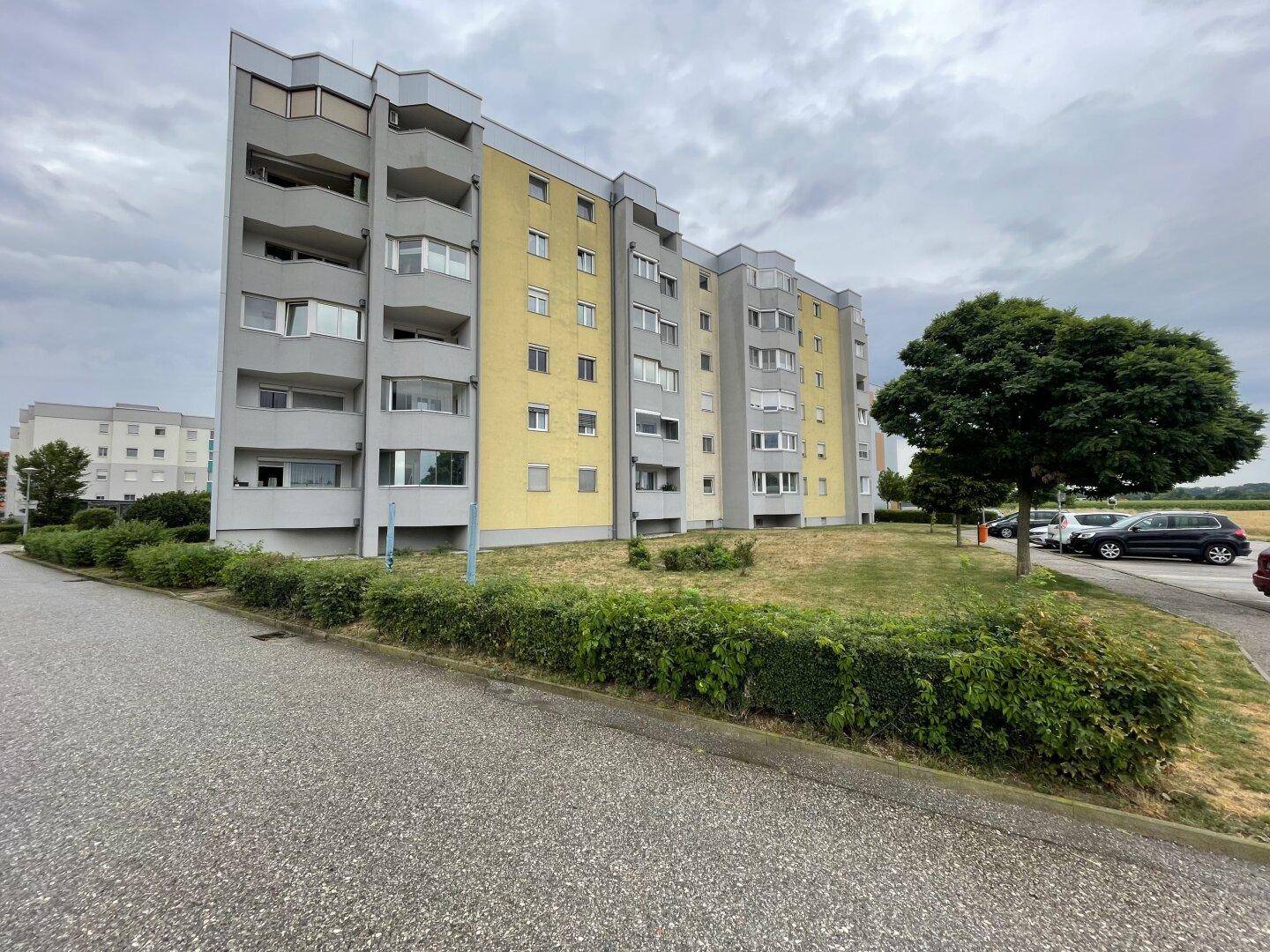 Lange Reihe von Mehrfamilienhäusern mit gelben und grauen Fassaden und Grünflächen davor.