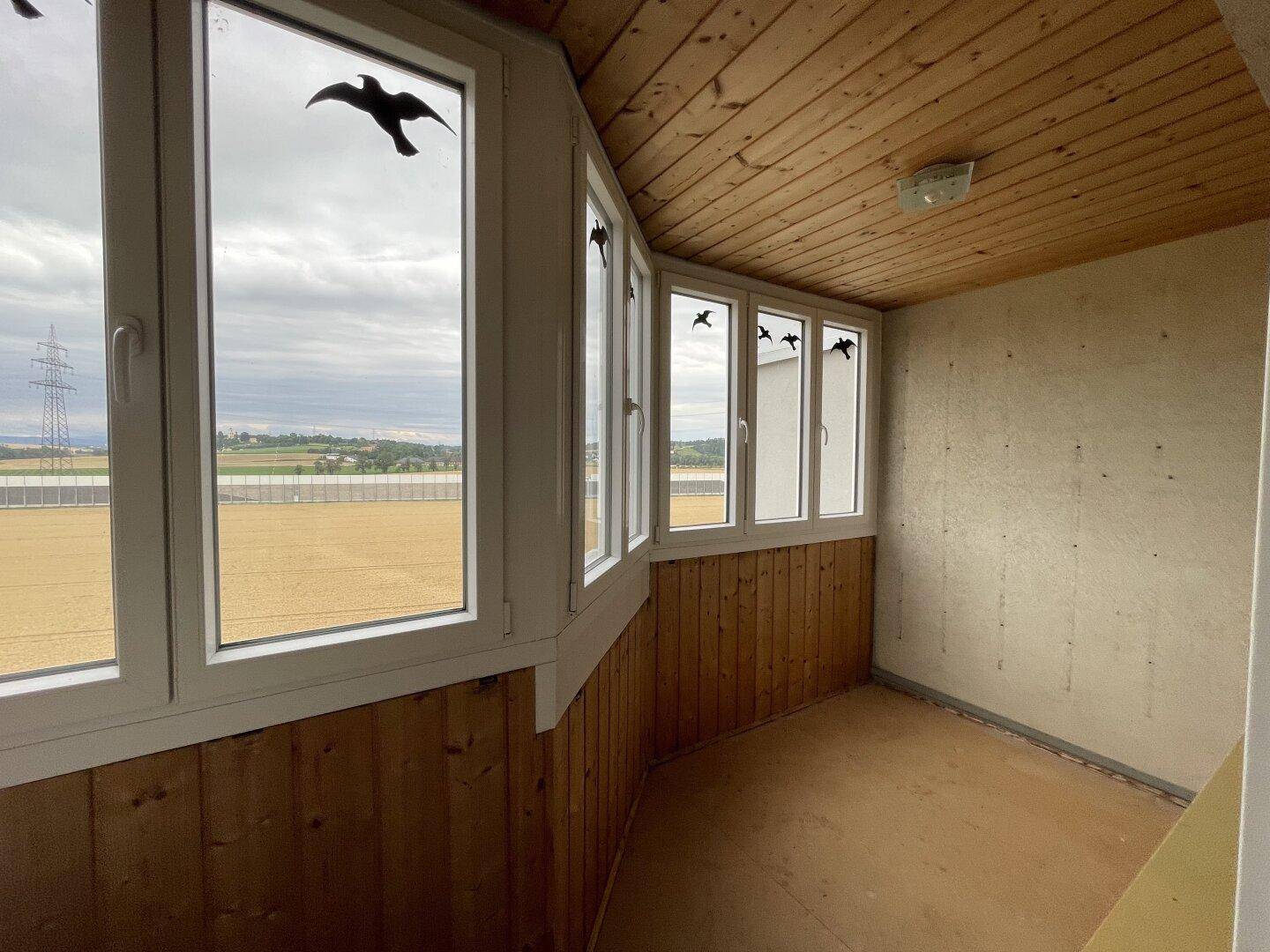 Verglaste Loggia mit Holzverkleidung an Wänden und Decke sowie weitem Blick über die Landschaft.