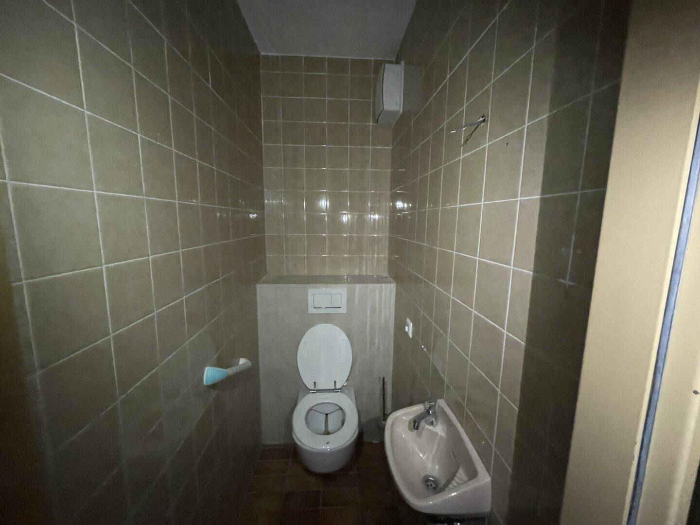 Kleines WC mit beigefarbenen Fliesen, wandhängender Toilette und Handwaschbecken.