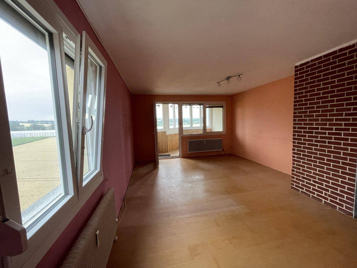 Geräumiges Wohnzimmer mit farbigen Wänden, Heizkörpern und Zugang zu einer verglasten Loggia.