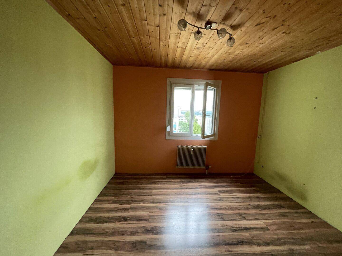 Unmöblierter Raum mit Holzdecke, farbigen Wänden und Fenster mit Blick ins Grüne.