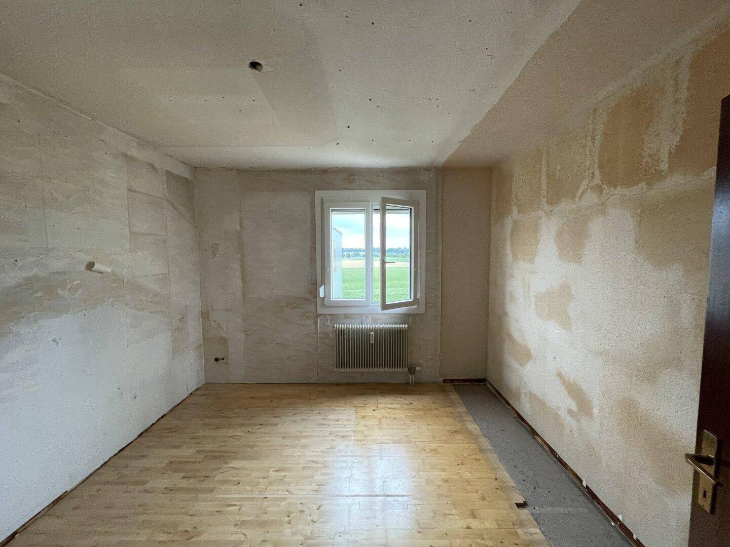 Unmöblierter Raum mit abgelöster Tapete, Holzboden und Fenster mit weitem Landschaftsblick.