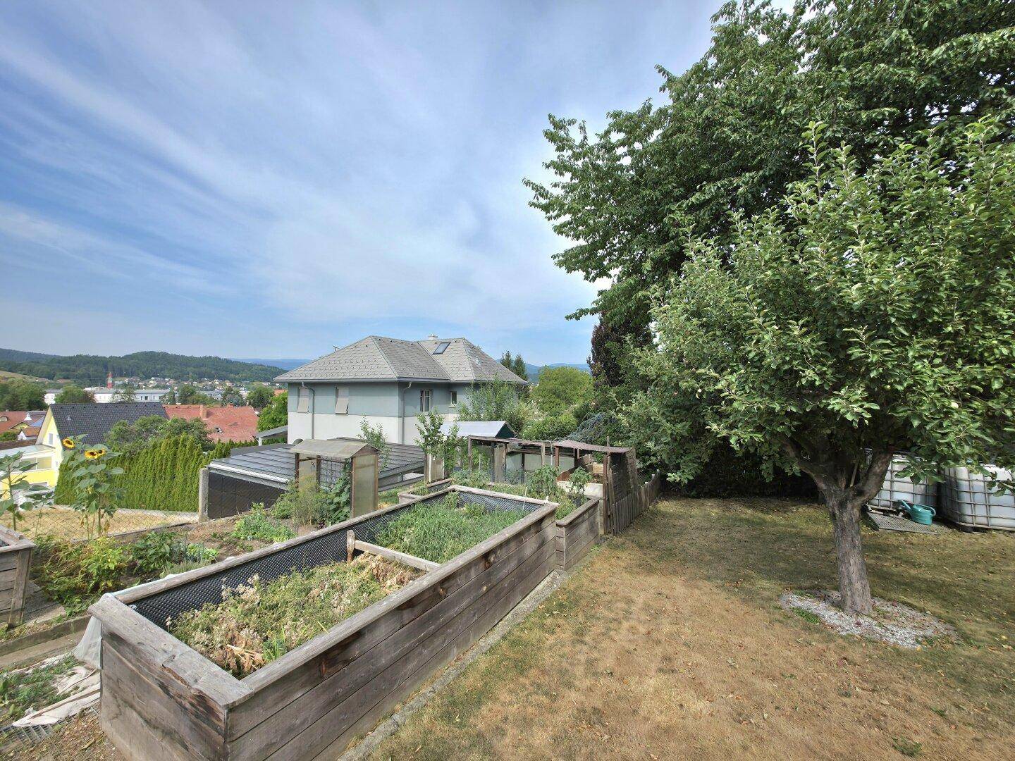 Nutzgarten mit Hochbeeten, Obstbäumen und Panoramablick über die ländliche Umgebung.