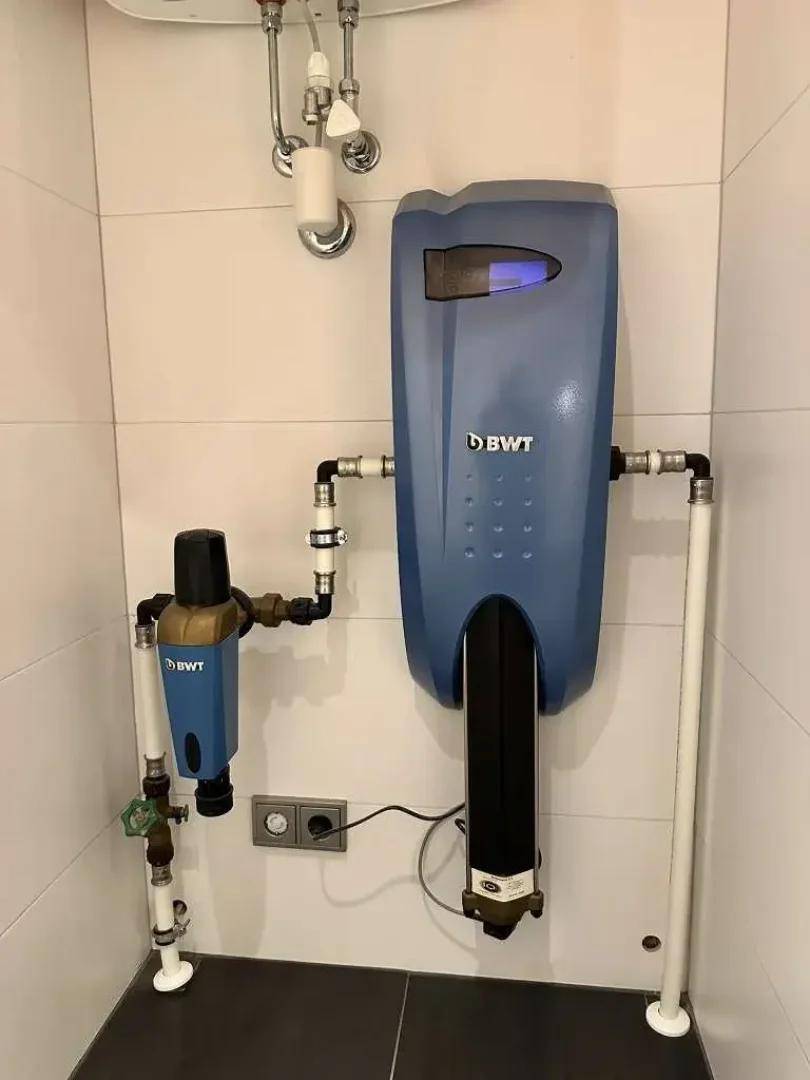 Wasseraufbereitungsanlage von BWT mit sichtbaren Rohren und Fliesenwand in einem Hauswirtschaftsraum.