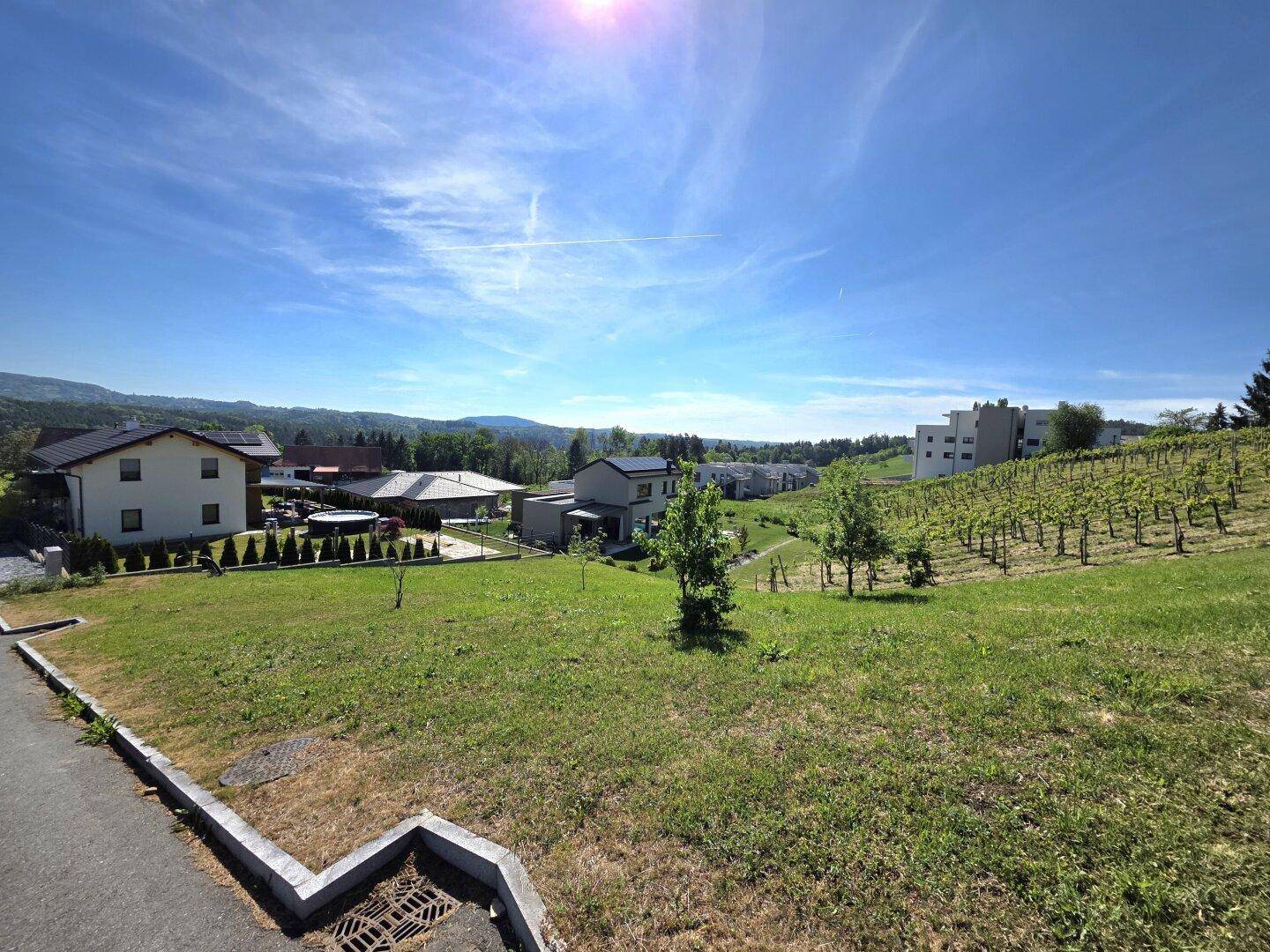 Weitläufige Aussicht auf eine Wohnsiedlung mit Weinbergen und grüner Landschaft unter blauem Himmel.