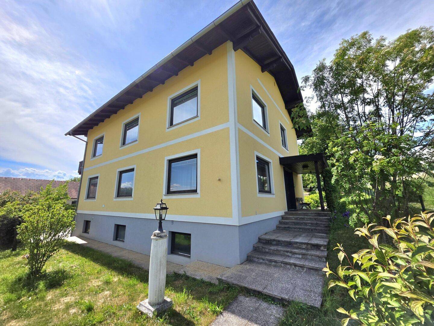 Gelbes Haus mit grauer Basis, Außentreppe und traditioneller Architektur unter blauem Himmel.