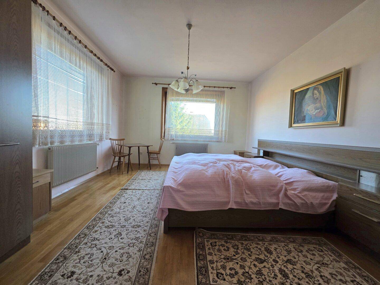 Helles Schlafzimmer mit Doppelbett, Holzmöbeln und Teppichen auf Parkettboden.