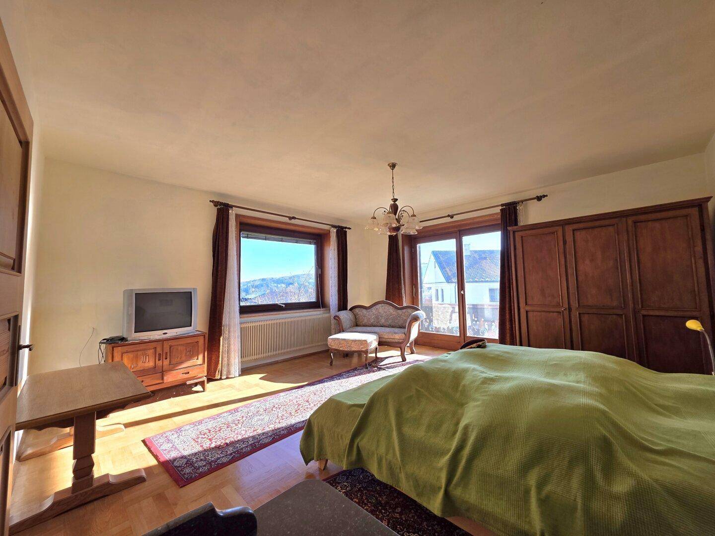 Gemütliches Schlafzimmer mit Doppelbett, traditionellen Möbeln und Blick ins Grüne.