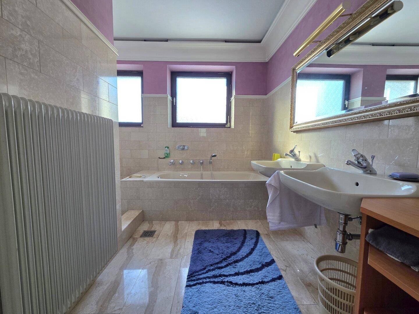 Geräumiges Badezimmer mit Doppelwaschbecken, Badewanne und hellen Fliesen.