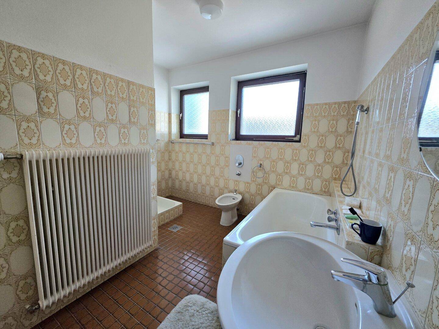 Badezimmer mit Badewanne, Bidet, Waschbecken und gemusterten Wandfliesen.