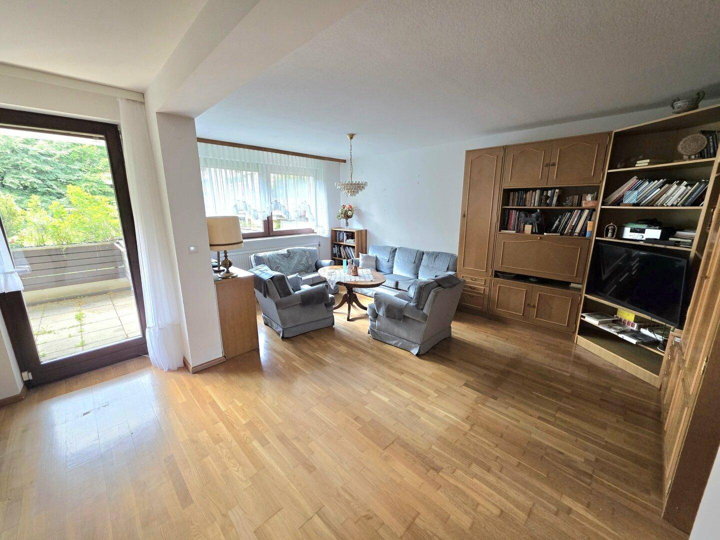 Helles Wohnzimmer mit Parkettboden, gemütlichen Sitzmöbeln und Zugang zum Balkon.