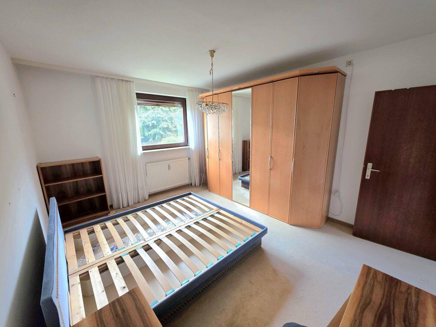 Geräumiges Schlafzimmer mit Teppichboden, großem Kleiderschrank und Fenster mit Grünblick.