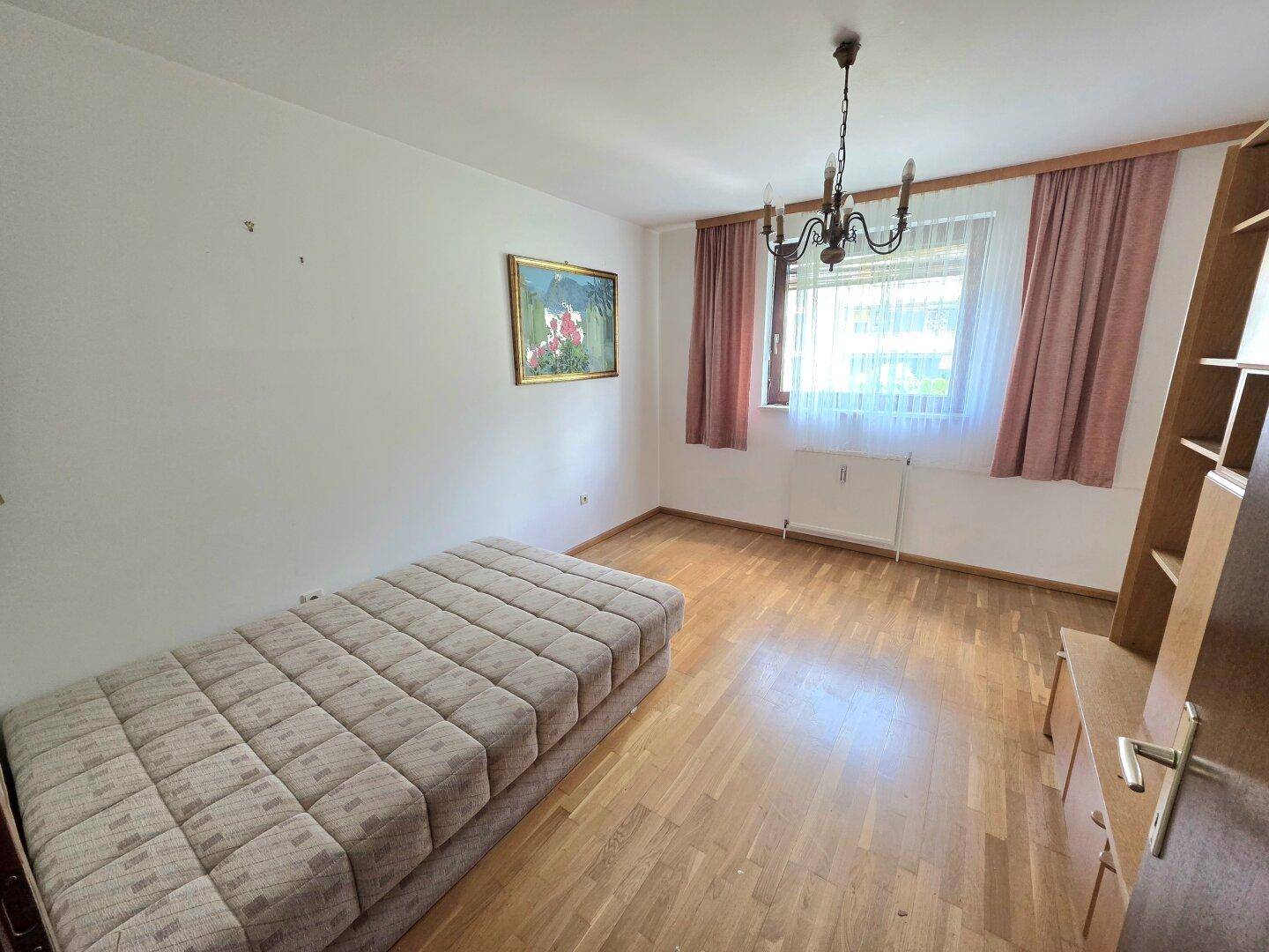 Gemütliches Schlafzimmer mit Parkettboden, Einzelbett und Fenster mit Vorhängen.