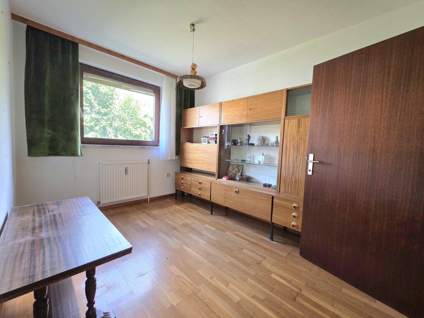 Helles Arbeitszimmer mit Parkettboden, Holzmöbeln und Fenster mit Blick ins Grüne.