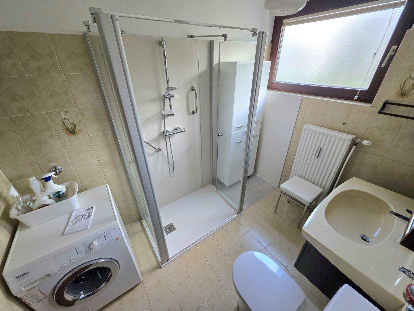 Funktionales Badezimmer mit Dusche, Waschbecken, WC und Waschmaschine.