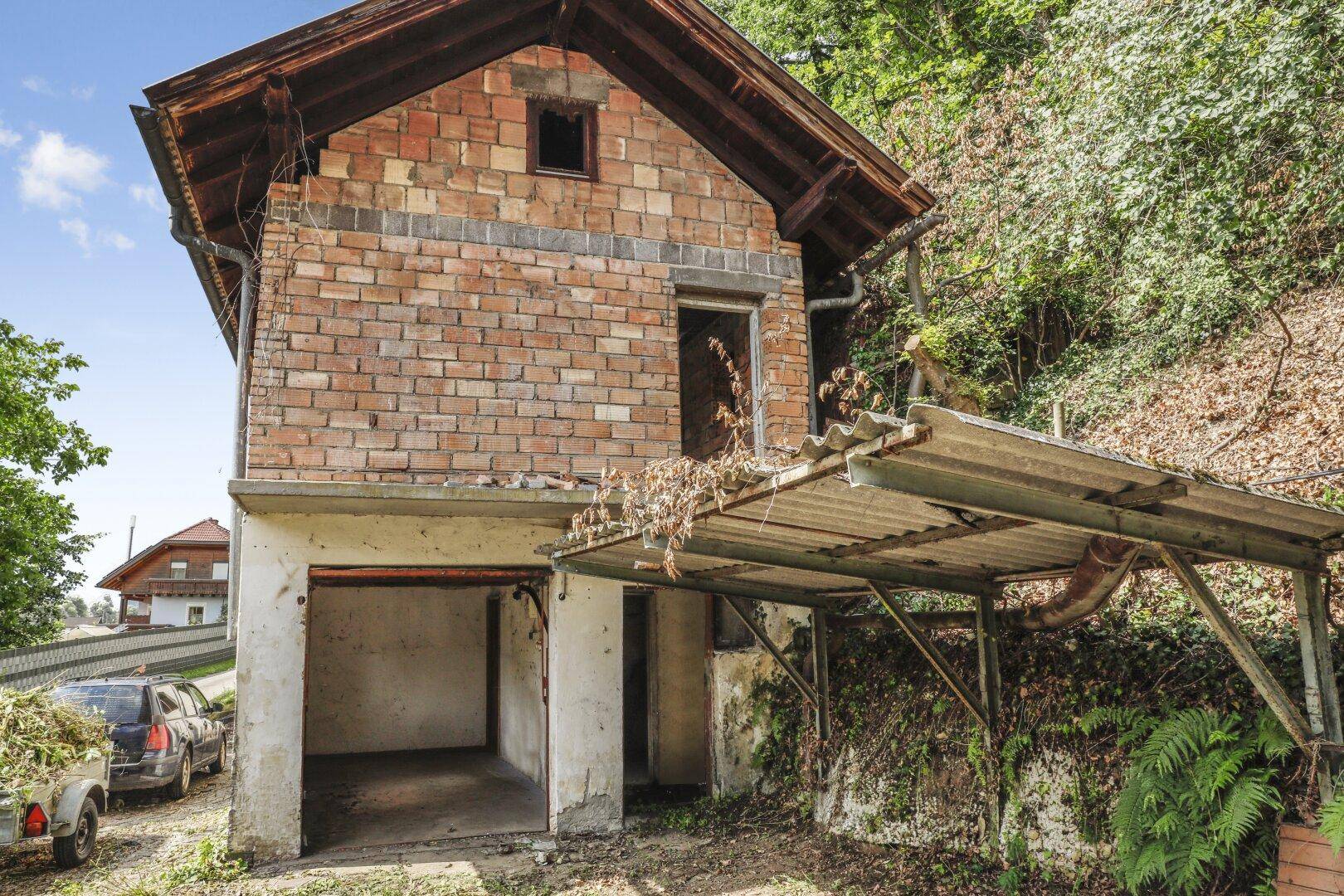Freiliegende Ziegelstruktur mit offener Garage und einfachem Carport, umgeben von Vegetation.