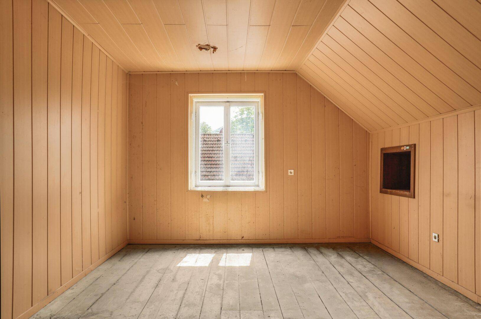 Leerer Dachbodenraum mit Holzvertäfelung an Wänden und Decke sowie Holzdielenboden.