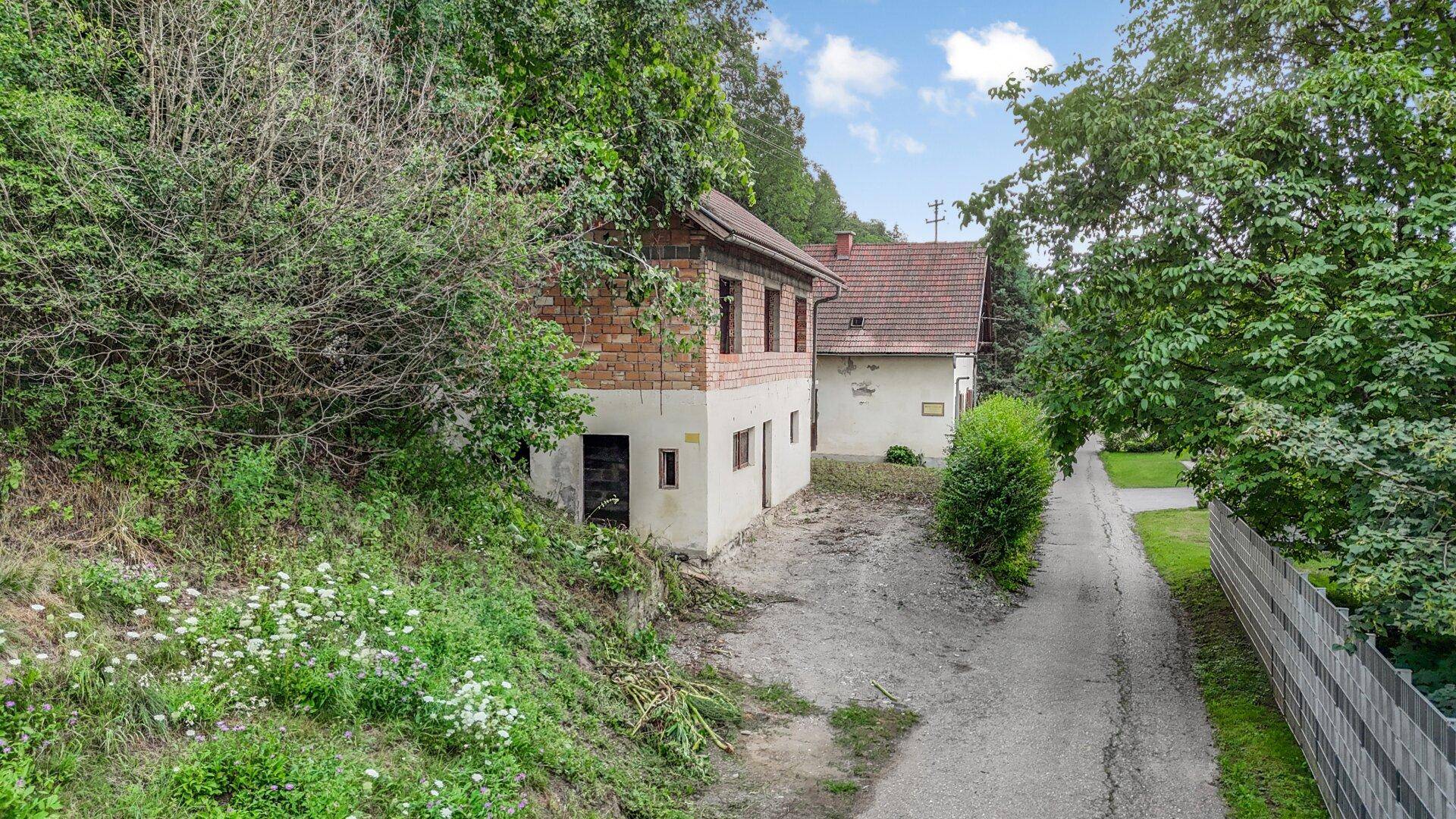Seitenansicht des Hauses mit freiliegendem Ziegelmauerwerk und weißer Fassade, umgeben von Vegetation.
