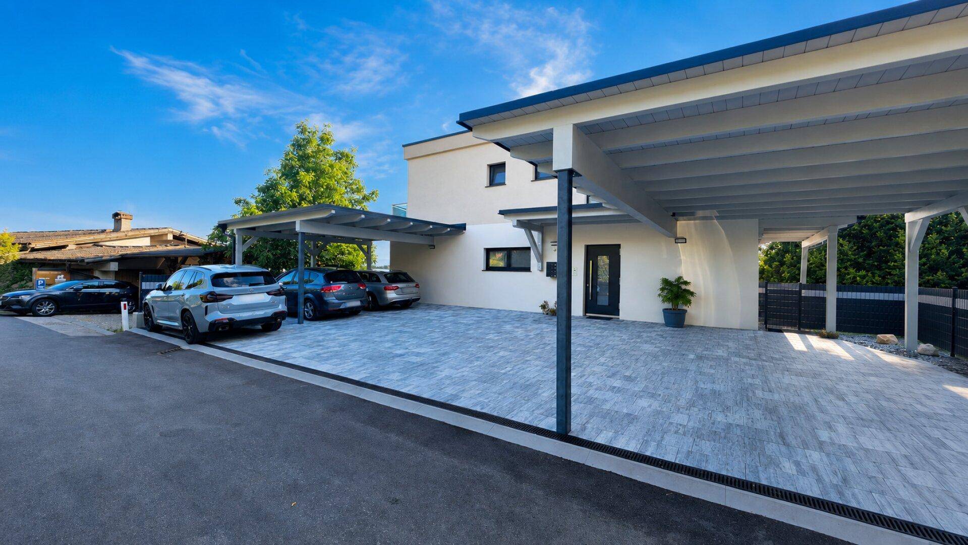 Modernes Gebäude mit mehreren Carports und gepflastertem Vorplatz unter blauem Himmel.