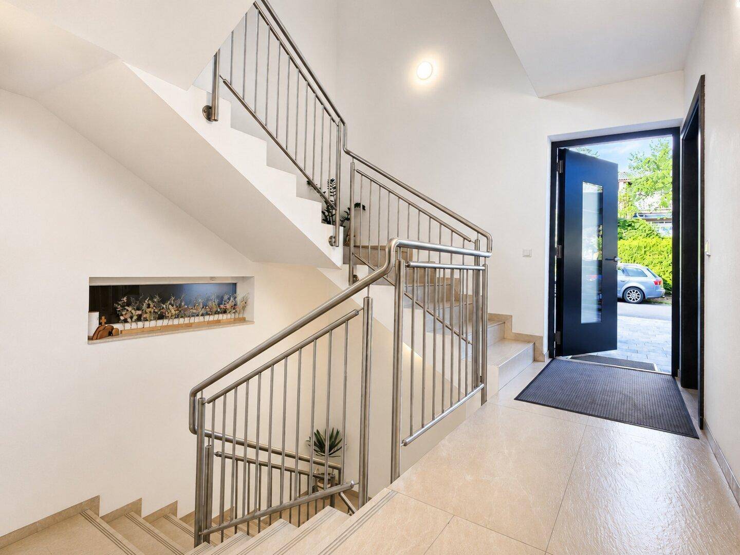 Eingangsbereich mit moderner Treppe aus Edelstahl und Fliesenboden, führt zu den oberen Etagen.