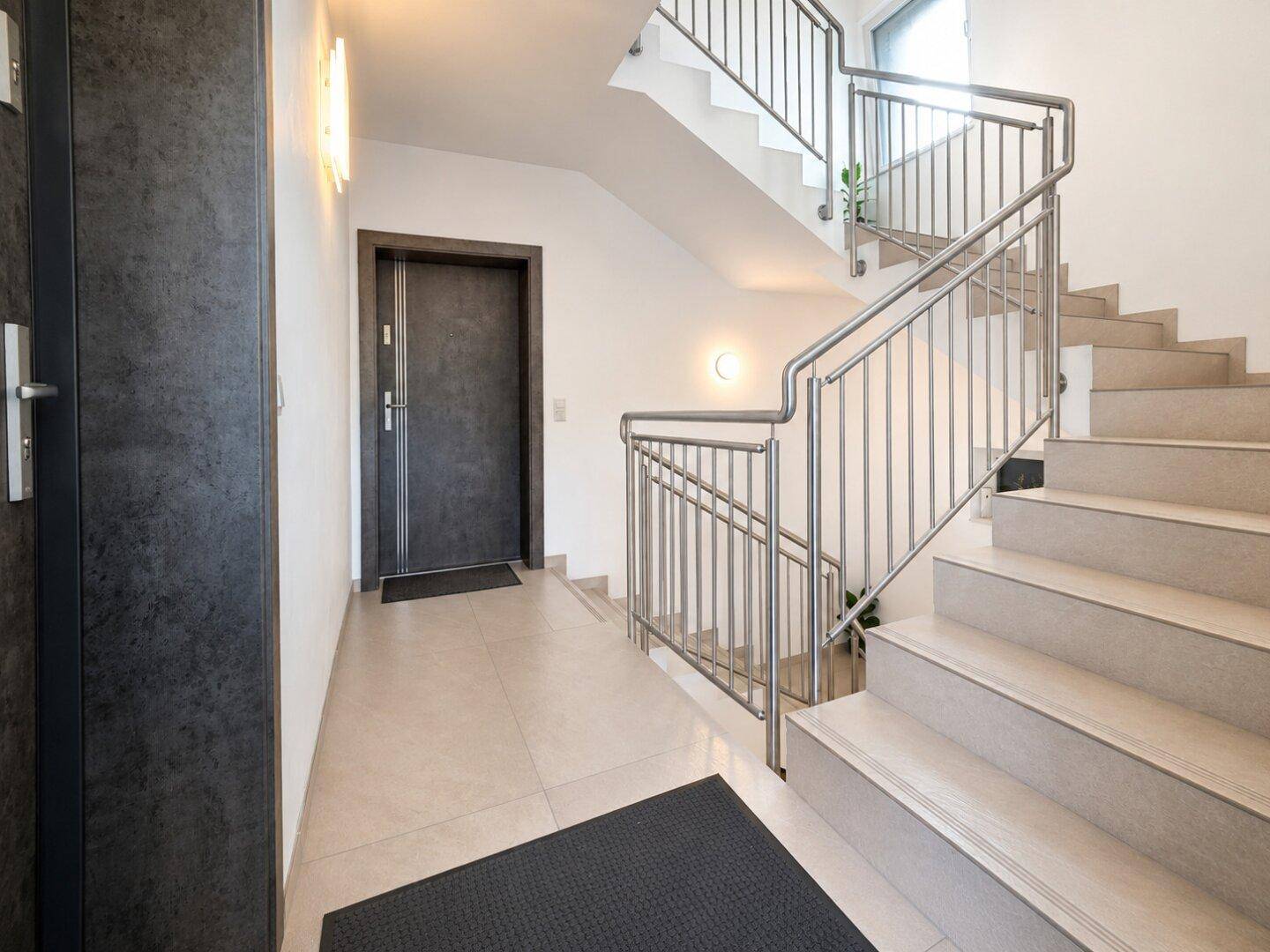 Treppenhaus mit Fliesenboden und Edelstahlgeländer, führt zu den verschiedenen Wohneinheiten.