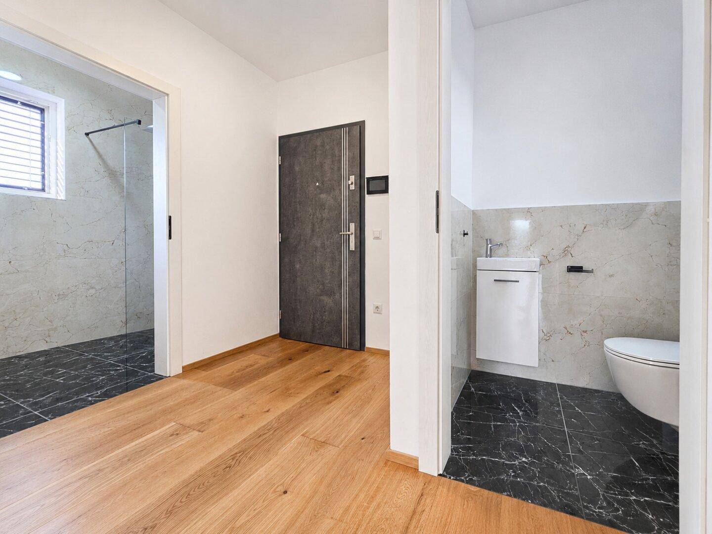 Heller Flur mit Holzboden, bietet Zugang zu einem modernen Badezimmer und einer separaten Toilette.
