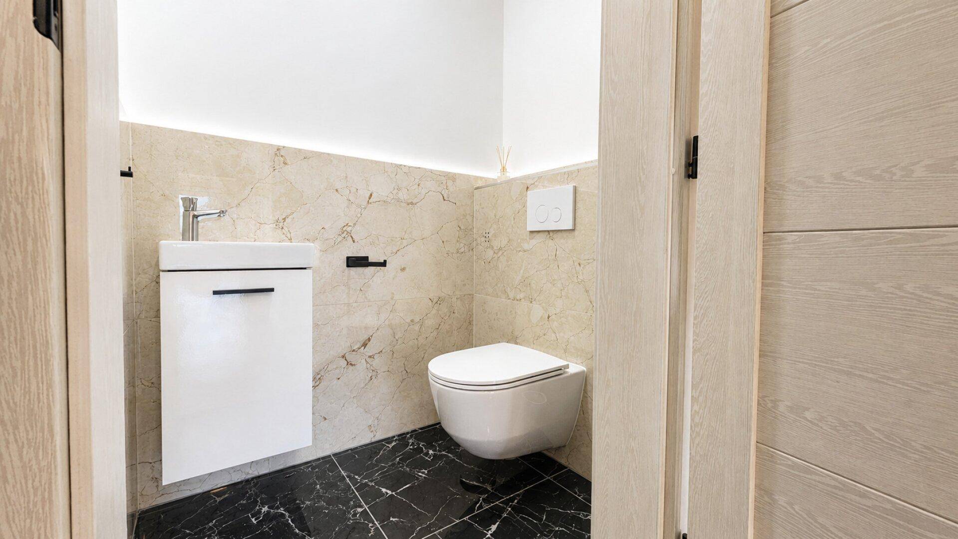 Modernes Gäste-WC mit schwarzem Marmorboden, wandhängender Toilette und kleinem Waschbecken.