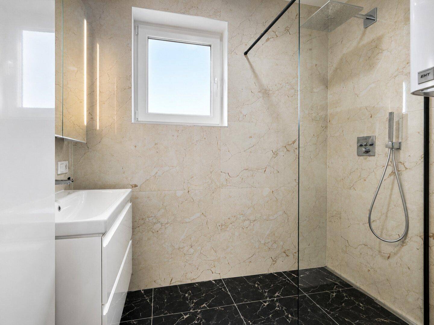 Modernes Badezimmer mit beigefarbenen Marmorfliesen, ebenerdiger Dusche und Fenster für Tageslicht.