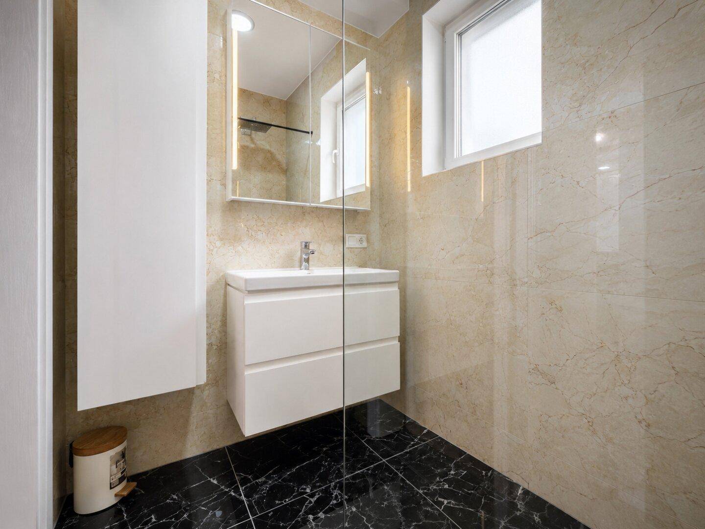 Helles Badezimmer mit beigefarbenen Marmorfliesen, modernem Waschtisch und beleuchtetem Spiegelschrank.