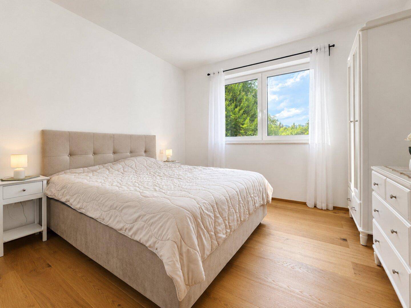 Helles Schlafzimmer mit Holzboden, großem Doppelbett und Fenster mit Blick ins Grüne.