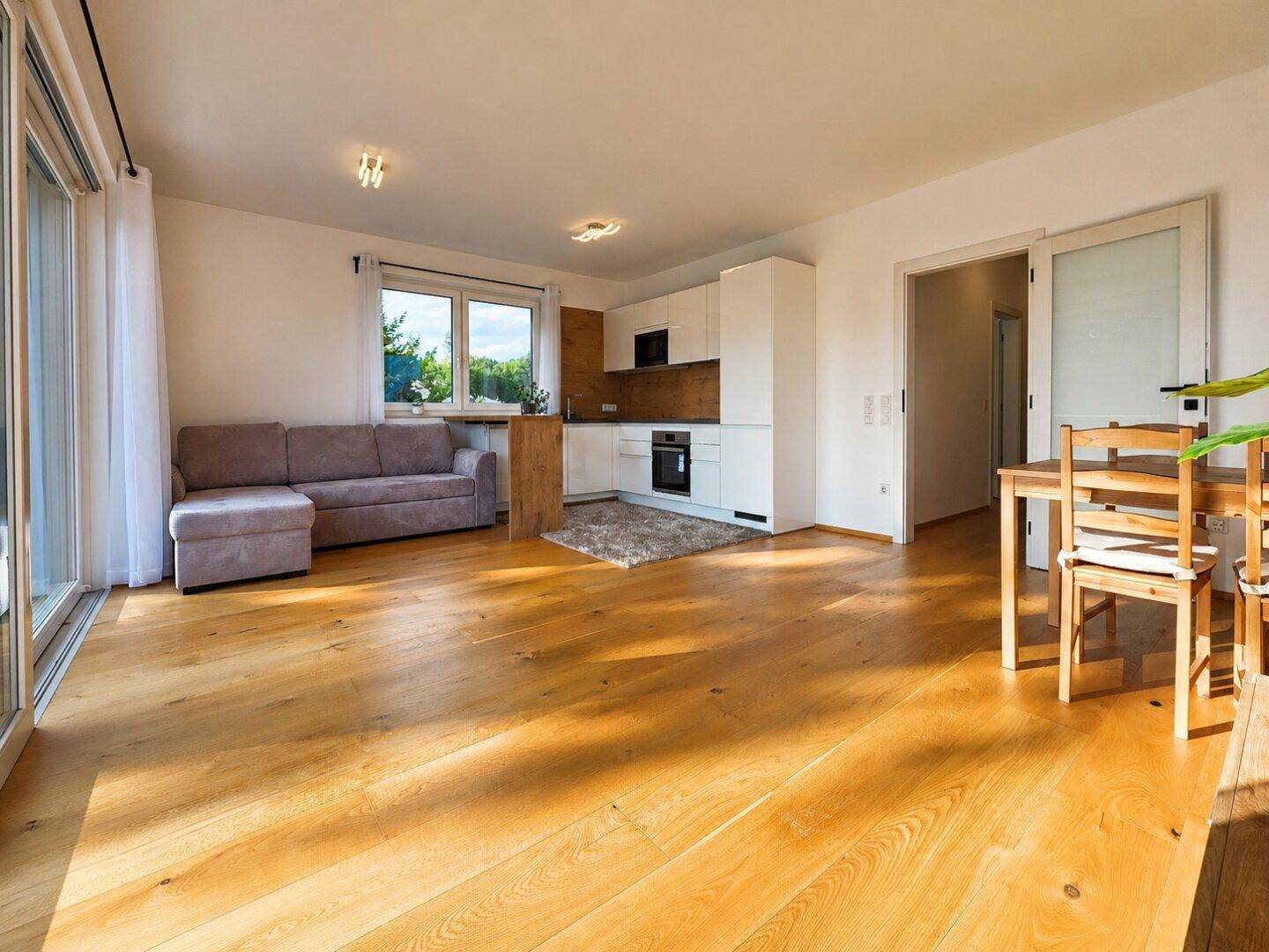 Lichtdurchfluteter Wohn-Essbereich mit offener Küche, Holzboden und Zugang zu einem Außenbereich.