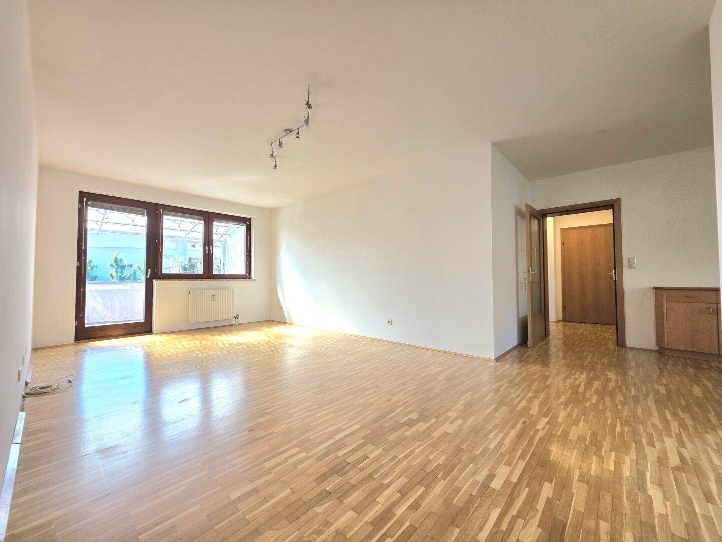 Geräumiges Wohnzimmer mit hellem Parkettboden und Zugang zu weiteren Räumen.