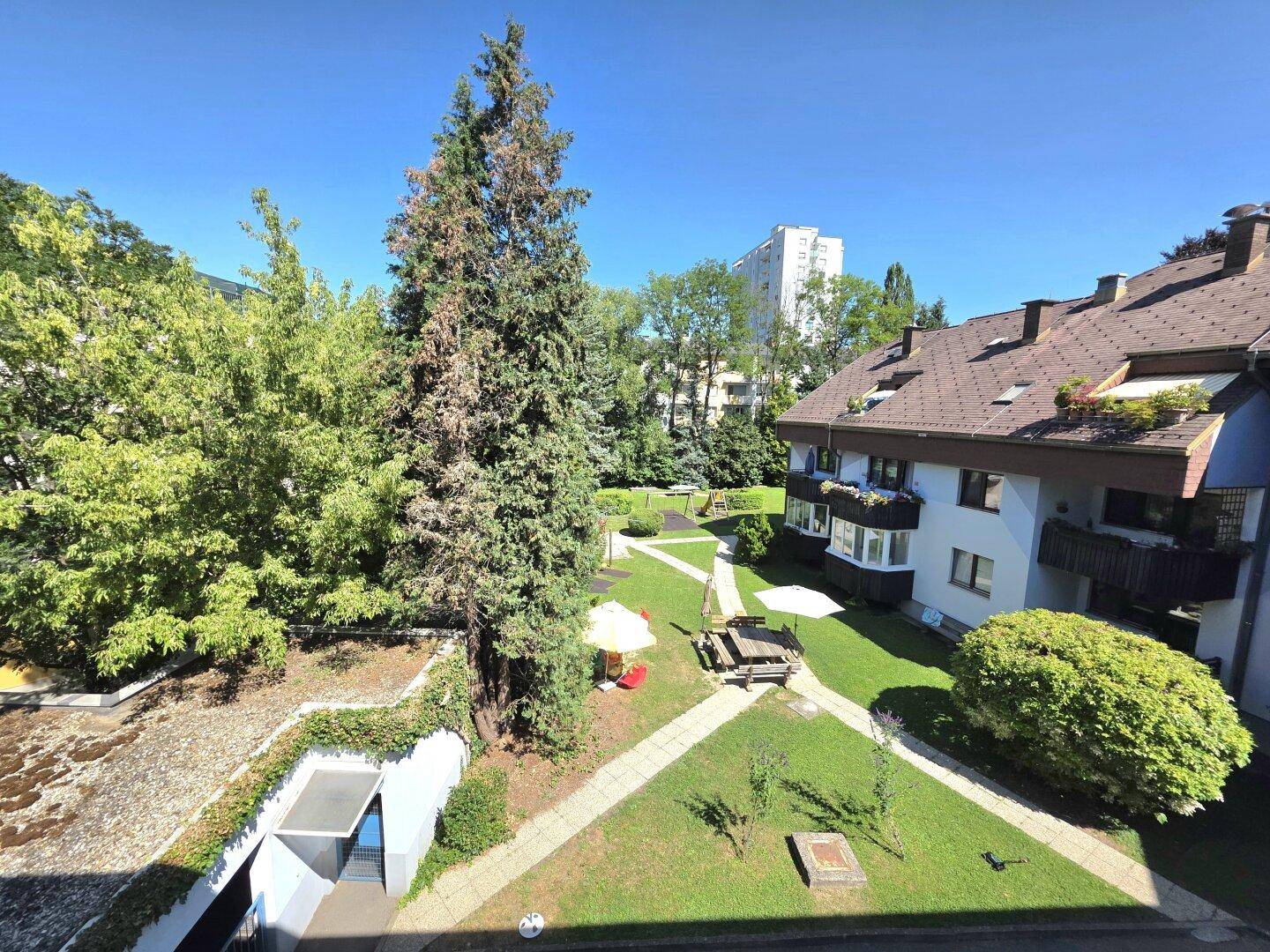 Gemeinschaftlicher Gartenbereich mit Rasenflächen, Bäumen und Spielplatz, umgeben von Wohngebäuden.