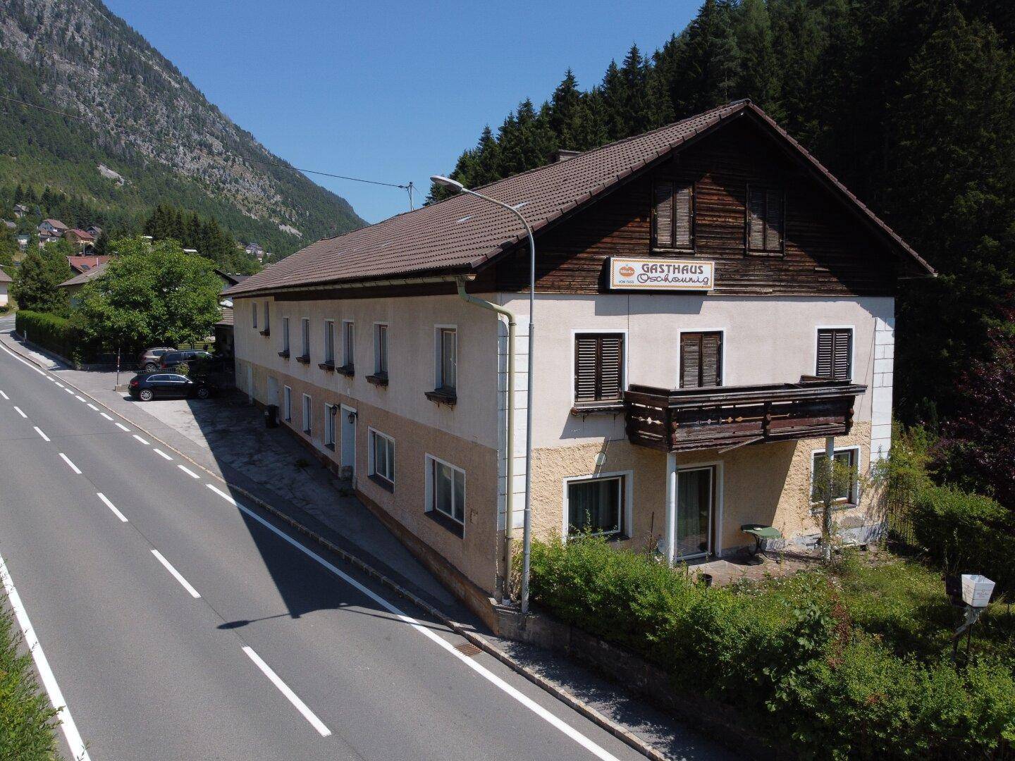 Ansicht des Gasthauses mit traditioneller Architektur, umgeben von alpiner Landschaft und einer Straße.