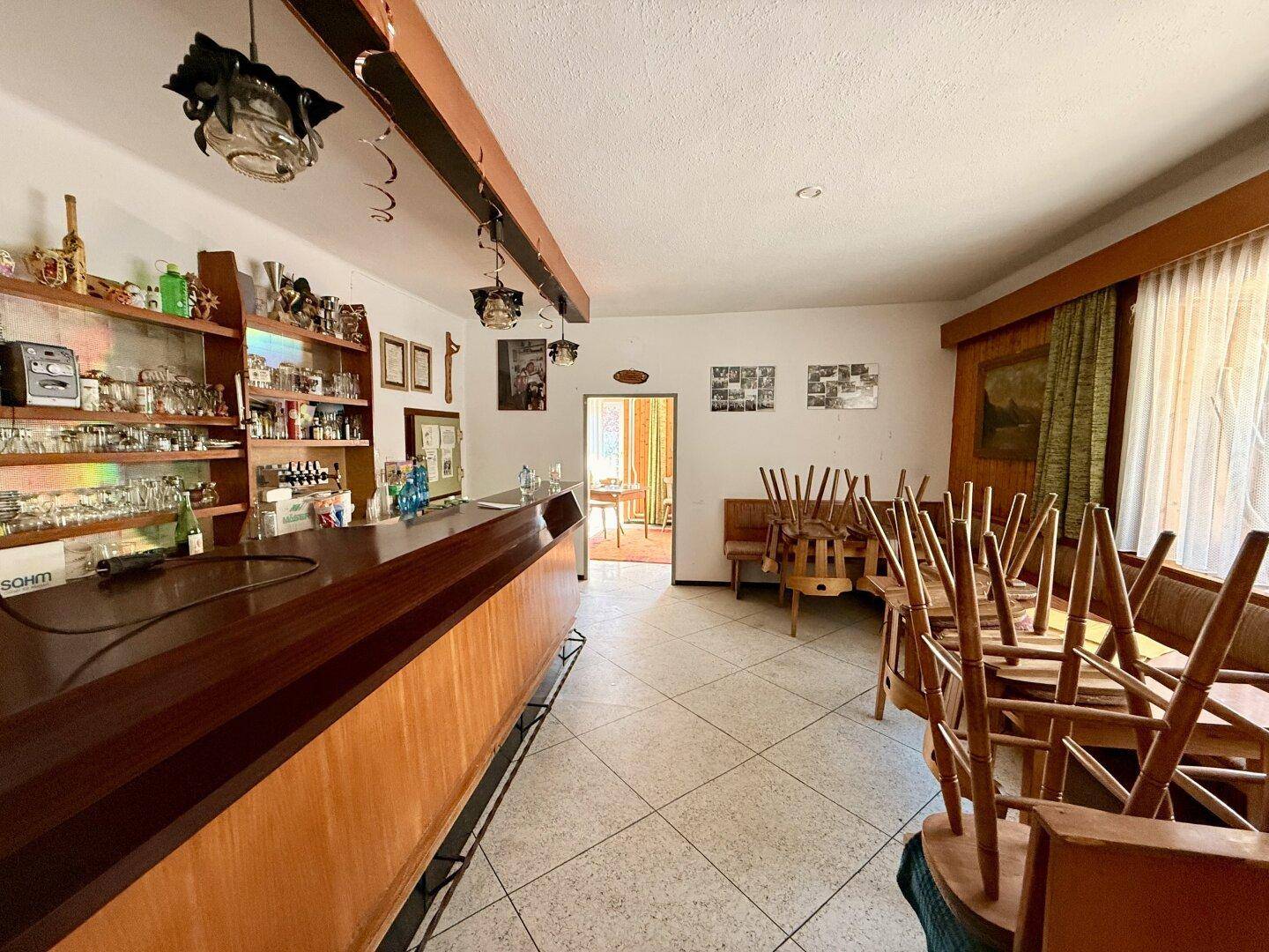 Traditioneller Barbereich mit Holztresen, gefliestem Boden und gestapelten Stühlen in einem Gasthaus.