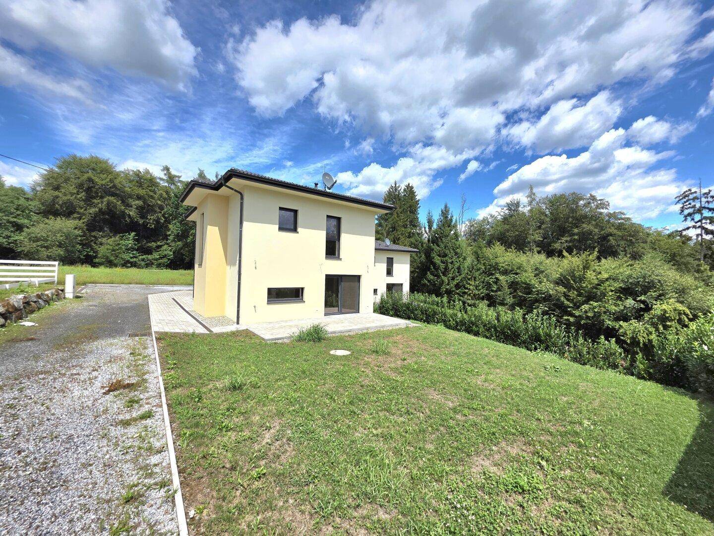 Neubau-Einfamilienhaus mit weitläufigem Rasen und Kiesauffahrt in ländlicher Umgebung.