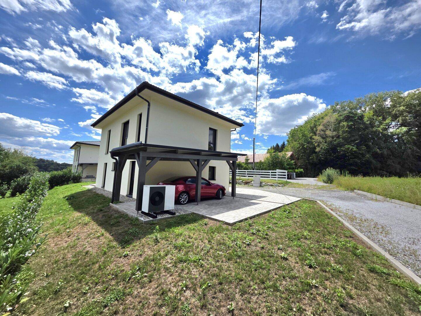 Modernes Einfamilienhaus mit Carport und Wärmepumpe, umgeben von Natur.