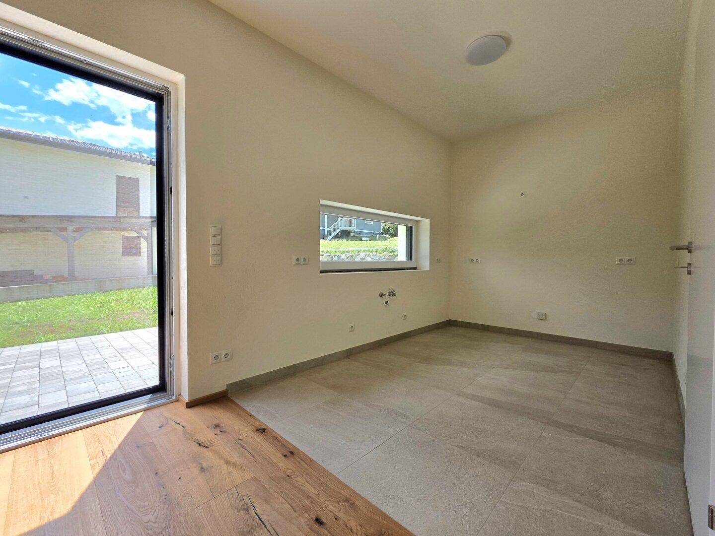Heller Raum mit Fliesenboden und Terrassenzugang, vorbereitet für eine Küche.