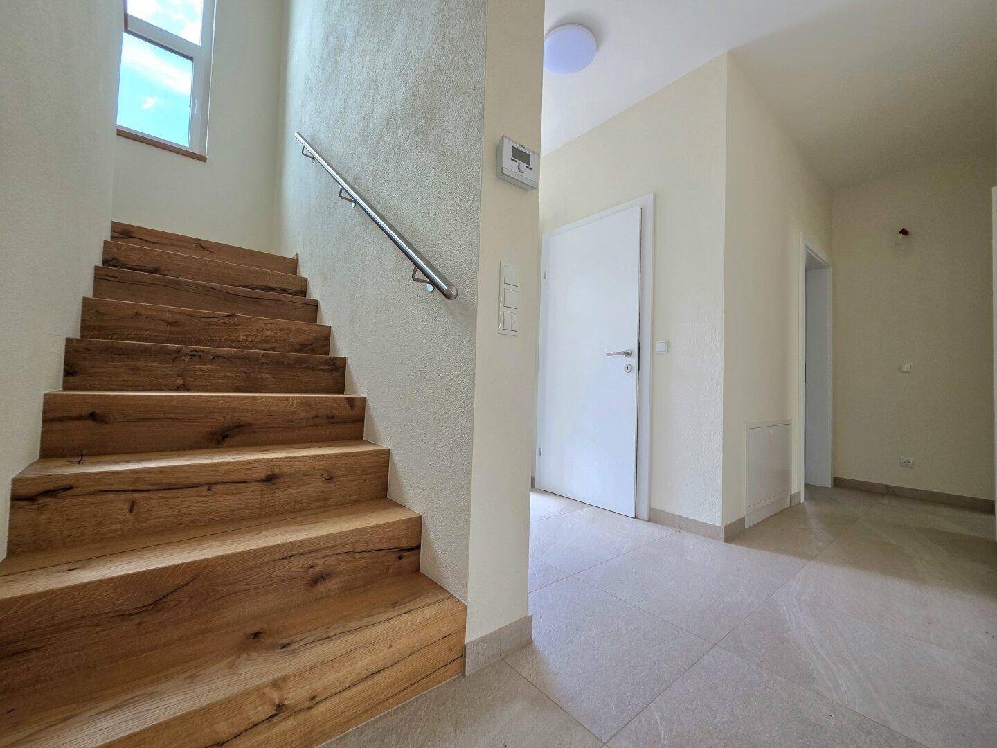 Moderne Holztreppe führt in die obere Etage, mit hellem Fliesenboden im Eingangsbereich.