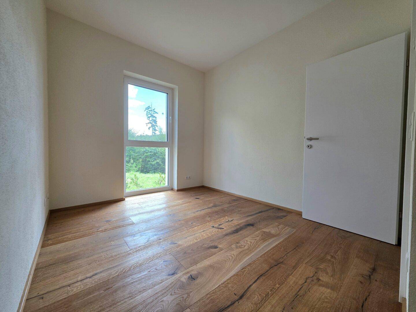 Gemütliches Schlafzimmer mit Holzboden und Fenster mit Blick in die Natur.