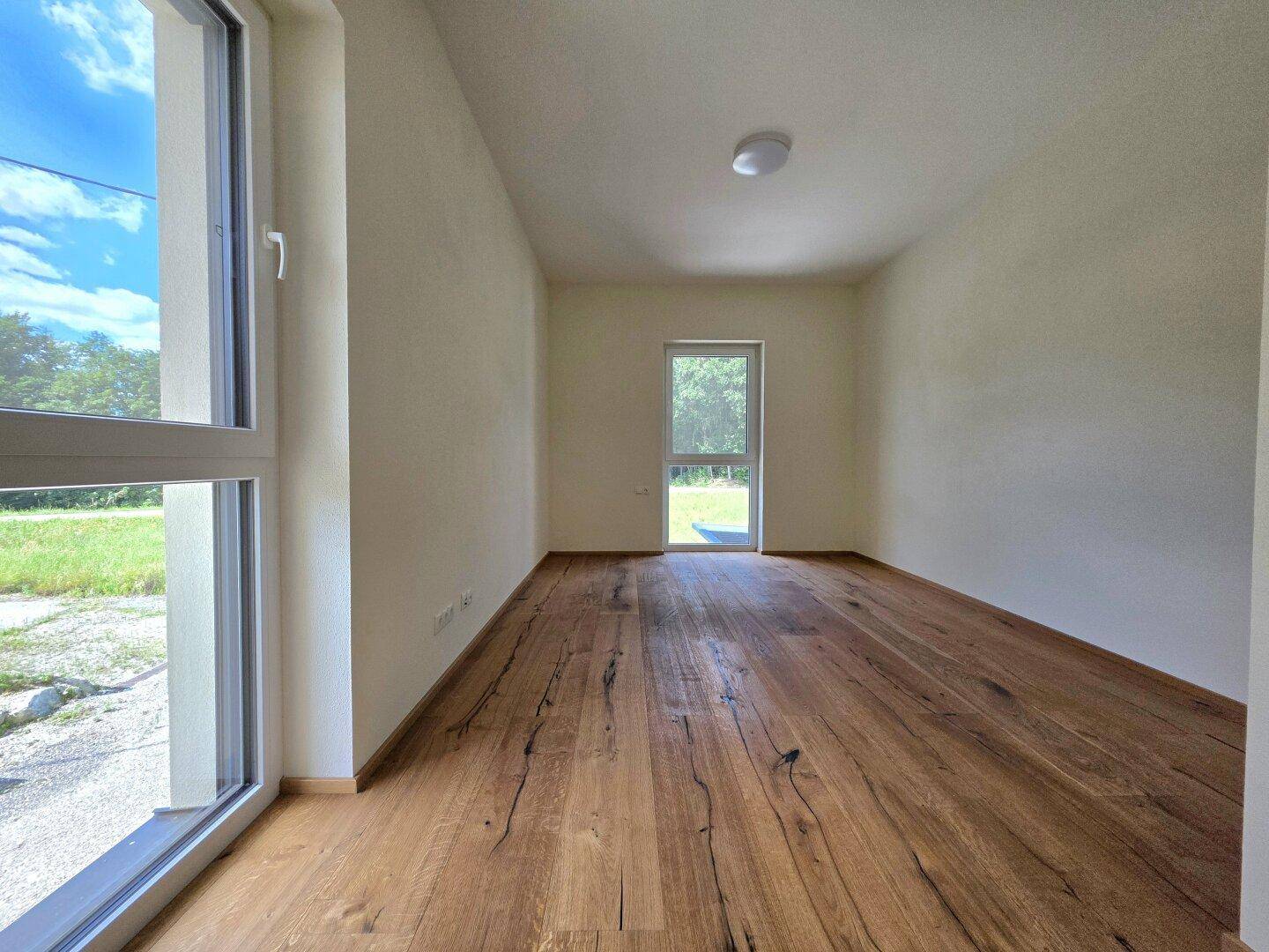 Helles Zimmer mit Holzboden und großen Fenstern, ideal als Schlaf- oder Arbeitszimmer.
