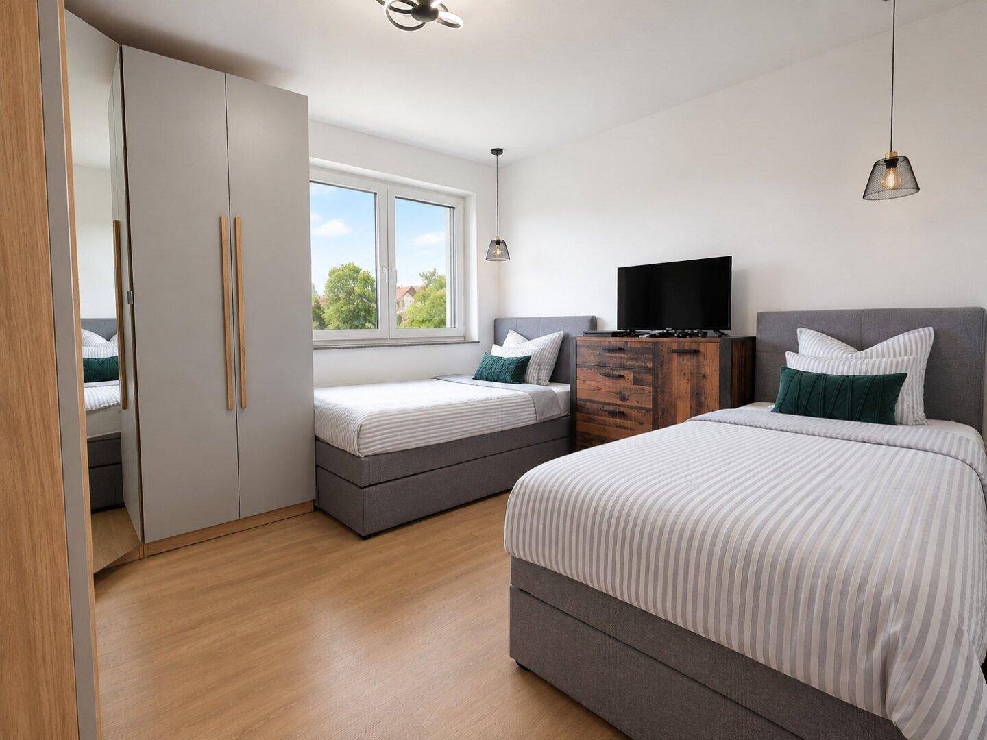 Helles Kinder- oder Gästezimmer mit zwei Einzelbetten, Kleiderschrank und Fernseher.
